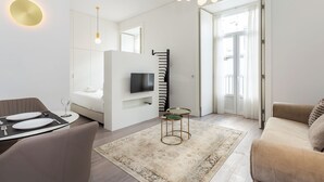 A modern hotel room with a dining area, a TV, a sofa, and a large window. - Morgan-Jupiter Apartments (Lisbon)