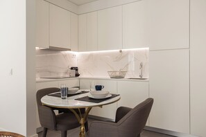 Uma cozinha moderna com armários brancos, uma moldura de backsplash de mármore e uma mesa de jantar redonda com duas cadeiras.