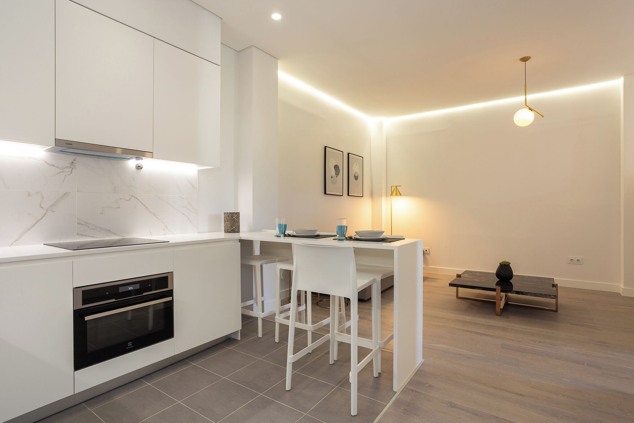 A modern kitchen with white cabinetry, a built-in oven, and a dining area with a bench and chairs.