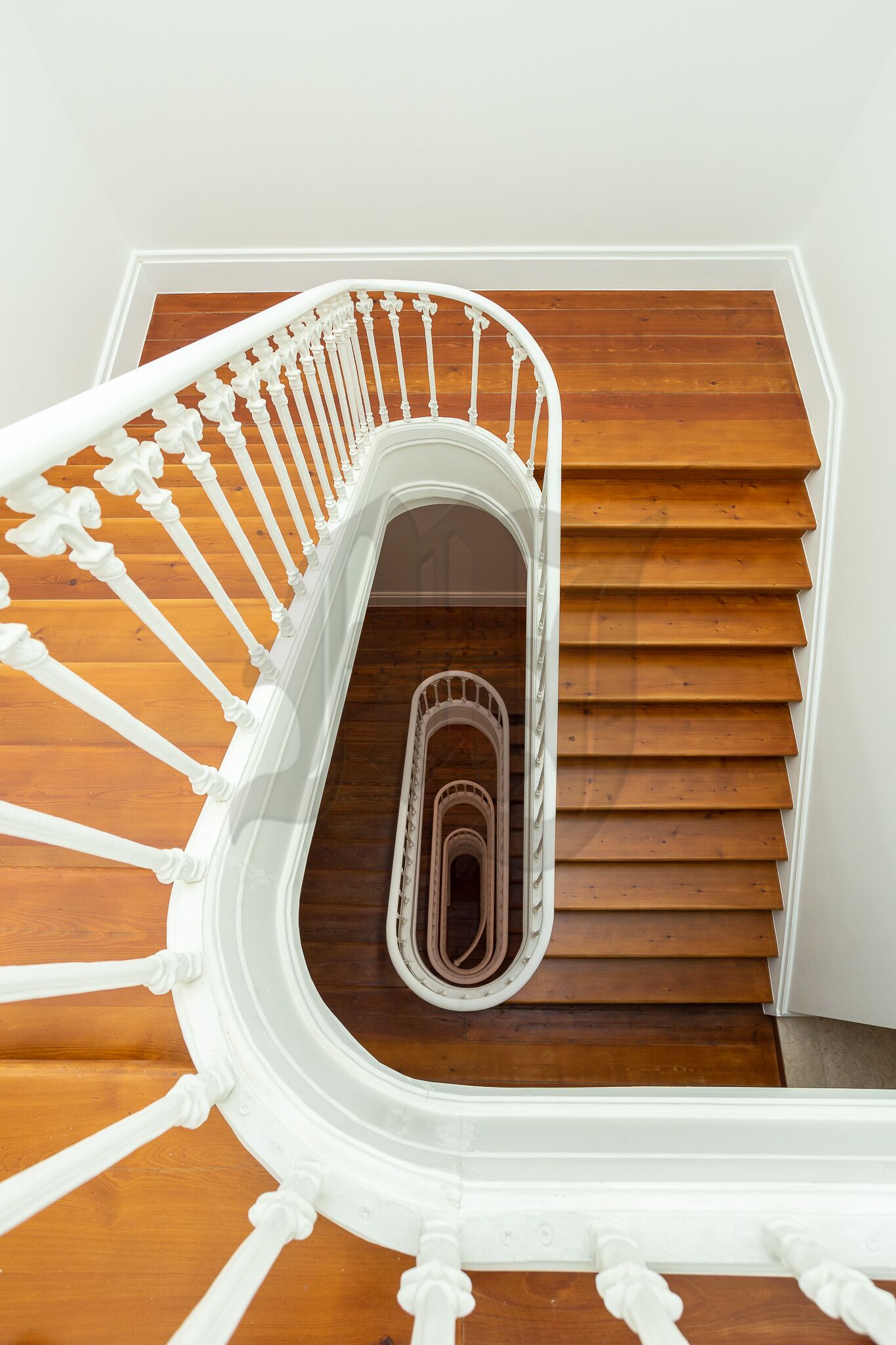 Un escalier en colimaçon avec des balustrades blanches et des marches en bois.