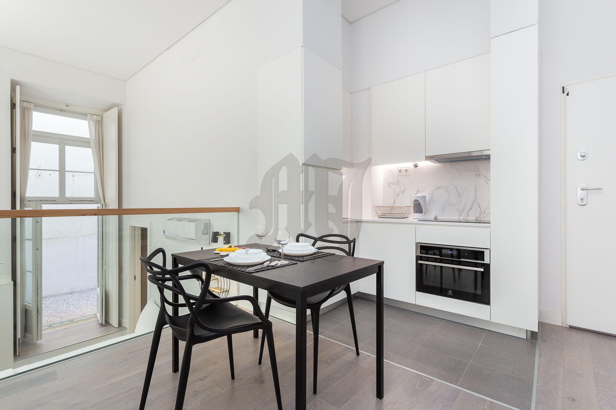 A modern kitchen with white cabinets, a built-in oven, and a dining area with a dark wooden table and chairs.