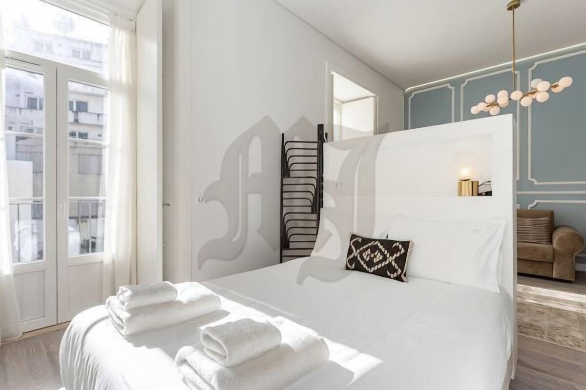 A hotel room with a large bed, a view through a glass door, and a chandelier.