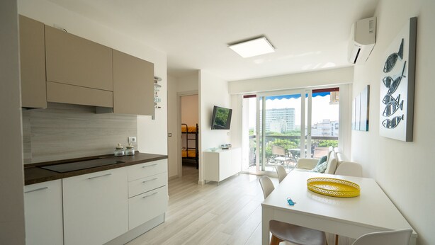 A modern kitchen with white cabinets, a dining area with a white table and chairs, and a balcony with a view of buildings. - Ariosto (Comacchio)