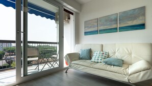 A modern living room with a beige sofa, a glass door leading to a balcony, and two paintings of a seascape on the wall. - Ariosto (Comacchio)