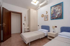 A bedroom with two beds, a wardrobe, a chair, and a painting on the wall. - Appartamento Darsena (Comacchio)