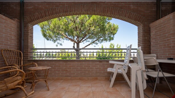 Une terrasse avec un mur en briques, une grande fenêtre, des chaises en osier et une table pliante blanche.