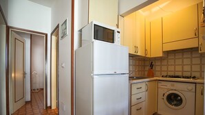 Une cuisine compacte équipée d’un réfrigérateur, d’un four à micro-ondes, d’un lave-linge et d’un crédence carrelée.