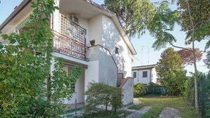 Une maison à deux étages avec un balcon, entourée de verdure et bordée d’un chemin en pierre.