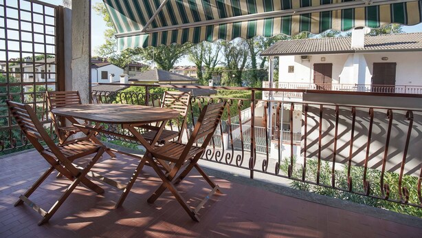 Un balcon avec une table et des chaises en bois, un auvent à rayures et une vue sur les maisons au loin.