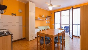 A compact kitchen with a dining area, a ceiling fan, and a view through the glass door. - Spinnaker (Comacchio)