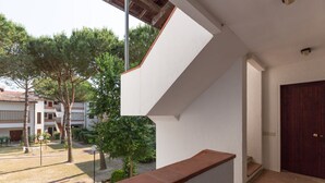 A modern building with a staircase leading to a dark wooden door, surrounded by trees and a clear sky. - Spinnaker (Comacchio)