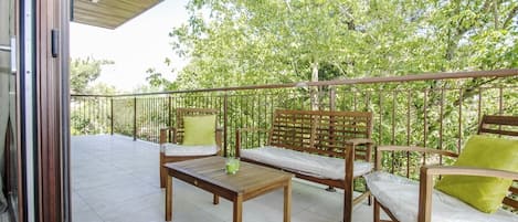 An outdoor balcony with wooden furniture, including a table and two chairs, and a metal railing.