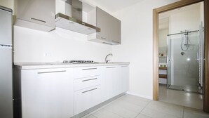A modern kitchen with white cabinets, a stainless steel range hood, and a glass shower enclosure. - Tasso (Ferrara)