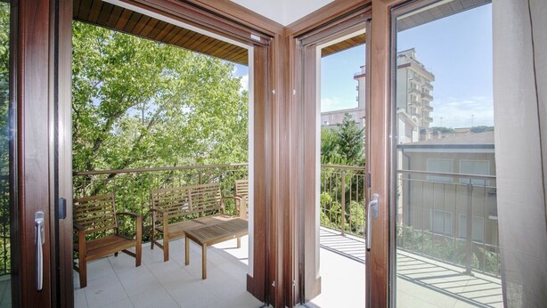 A balcony with wooden furniture and a view of greenery and buildings. - Tasso (Ferrara)