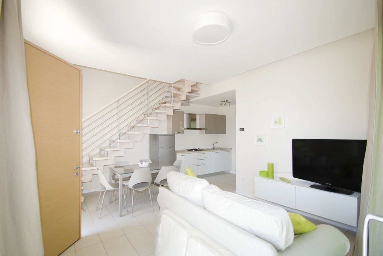 Um espaço de estar moderno e compacto, com escada que dá acesso a uma cozinha, área de jantar e sala de estar com televisão de tela plana.