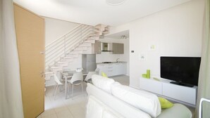 A modern, compact living space with a staircase leading to a kitchen, a dining area, and a living room with a flat-screen TV. - Tasso (Ferrara)