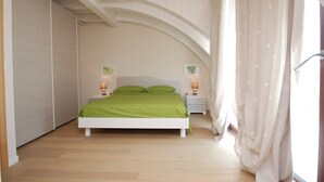 A bedroom with a bed, two bedside tables, a window with curtains, and a white ceiling. - Tasso (Ferrara)