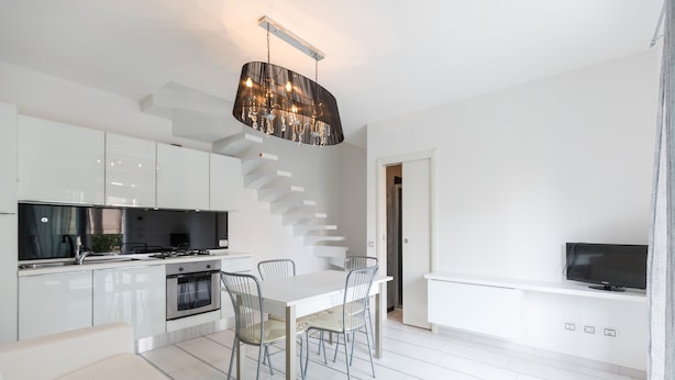 A modern kitchen with white cabinetry, a dining area with a white table and chairs, a built-in TV, and a staircase leading to another level. - Villa Marina (Comacchio)