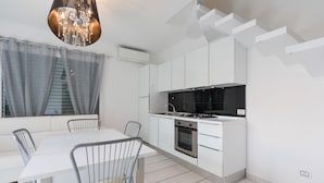 A modern kitchen with white cabinetry, a gas stove, and a dining area with a white table and metal chairs. - Villa Marina (Comacchio)