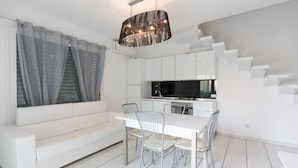 A modern kitchen with white cabinets, a dining table with chairs, and a staircase. - Villa Marina (Comacchio)