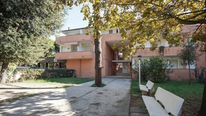 A courtyard with a pathway leading to a building with balconies. There are benches and trees in the area. - Appartamento Aurelia (Comacchio)