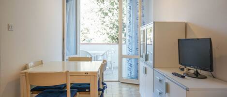 A small, bright room with a dining table, chairs, a television, and a sliding glass door leading to an outdoor area.