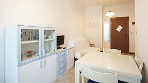 A compact kitchen with a dining area, a white cabinet with glass doors, a small table, and a chair. - Appartamento Aurelia (Comacchio)