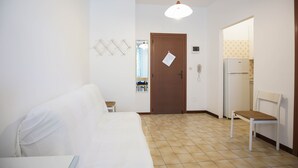 A hotel room with a bed, a chair, a door with a note, a mirror, and a refrigerator. - Appartamento Aurelia (Comacchio)