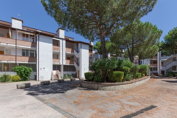 A multi-story residential building with balconies, a central courtyard with trees, and a no-parking sign.