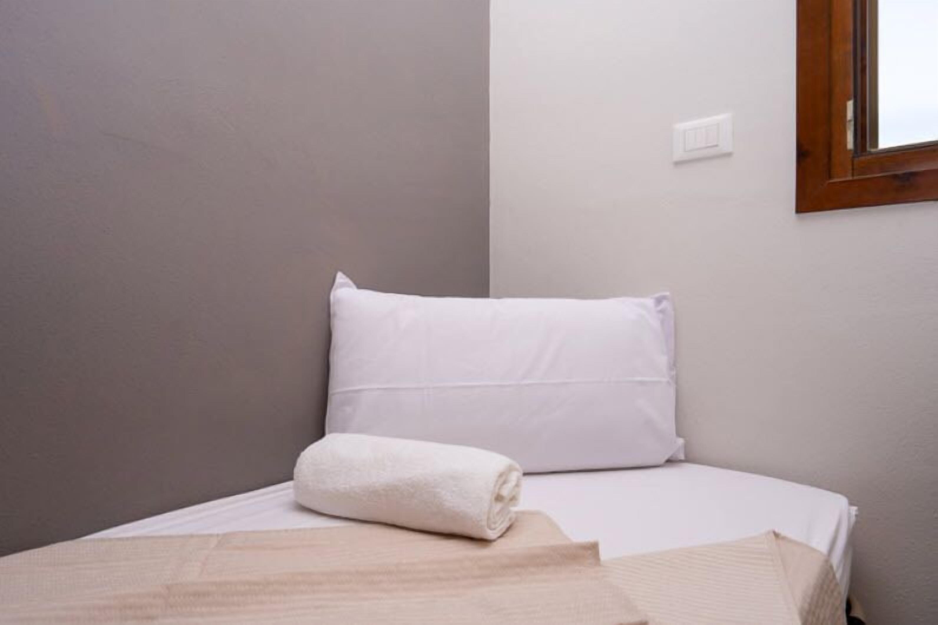 A single bed with white bedding and a rolled white towel.