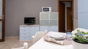 A dining area with a table set for two, a microwave on a cabinet, and a television on a dresser. - Residence Smith - Piano Terra 2A (Comacchio)