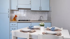 A modern kitchen with light blue cabinets, a white dining table set for four, and a small potted plant on the table. - Residence Smith - Piano Terra 2A (Comacchio)