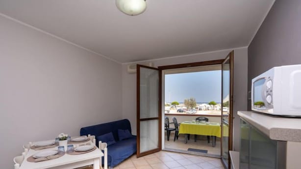 A compact living space with a dining area, a sofa, and a balcony with a table and chairs. - Residence Smith - Piano Terra 2A (Comacchio)