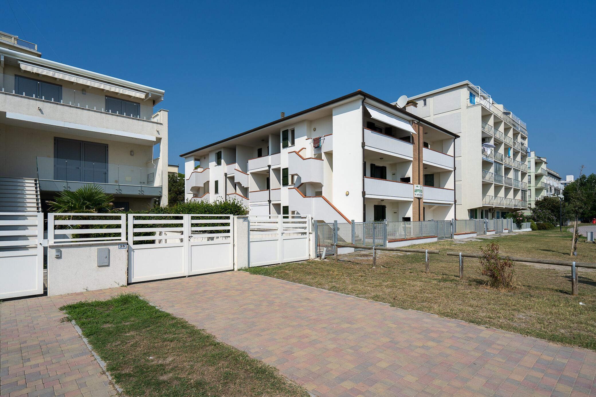 A modern apartment building with multiple balconies and a paved walkway.