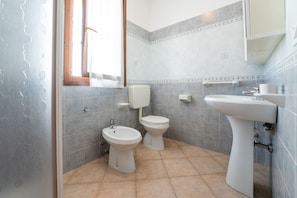 A bathroom with two toilets, a bidet, a sink, and a window with curtains.