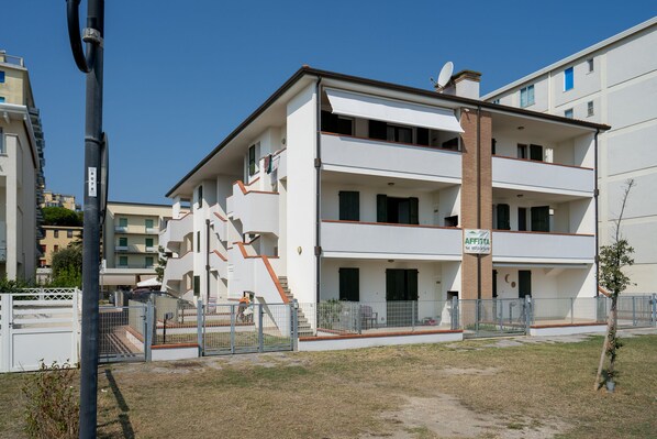 A multi-story residential building with a white facade, a visible staircase, and a balcony.