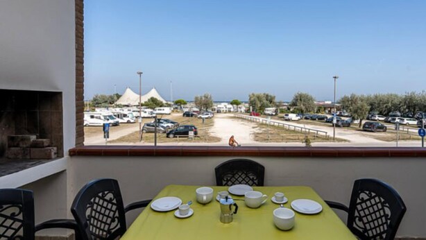 An outdoor dining area with a table set for four, overlooking a parking lot and a beach. - Residence Smith 2 Piano Laterale E 3C (Comacchio)