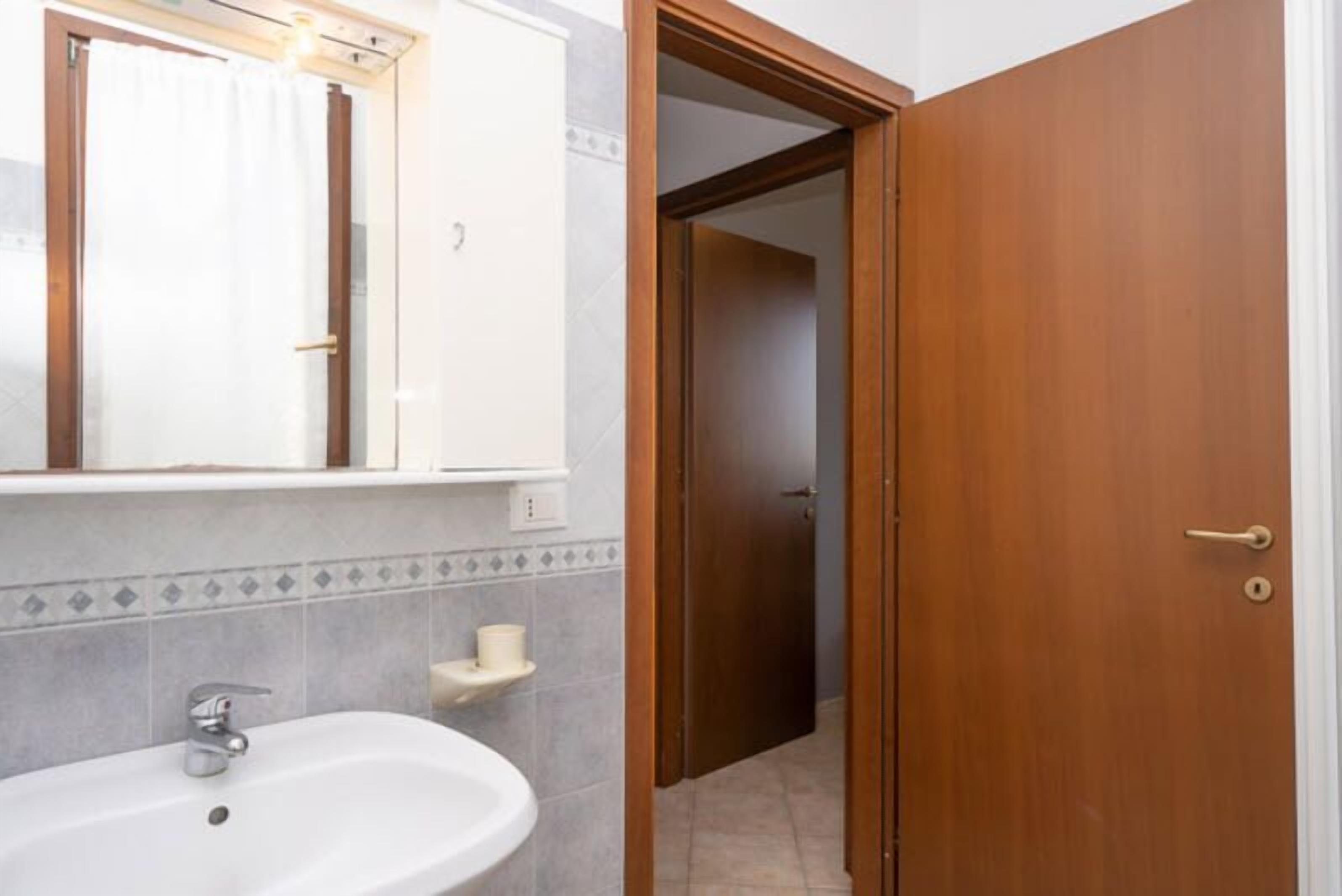 Un baño con lavamanos, espejo y puerta de madera que da a otra habitación.