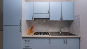 A kitchen with light blue cabinets, a gas stove, a sink, and a pair of orange oven mitts on the counter. - Residence Smith 2 Piano Laterale E 3C (Comacchio)