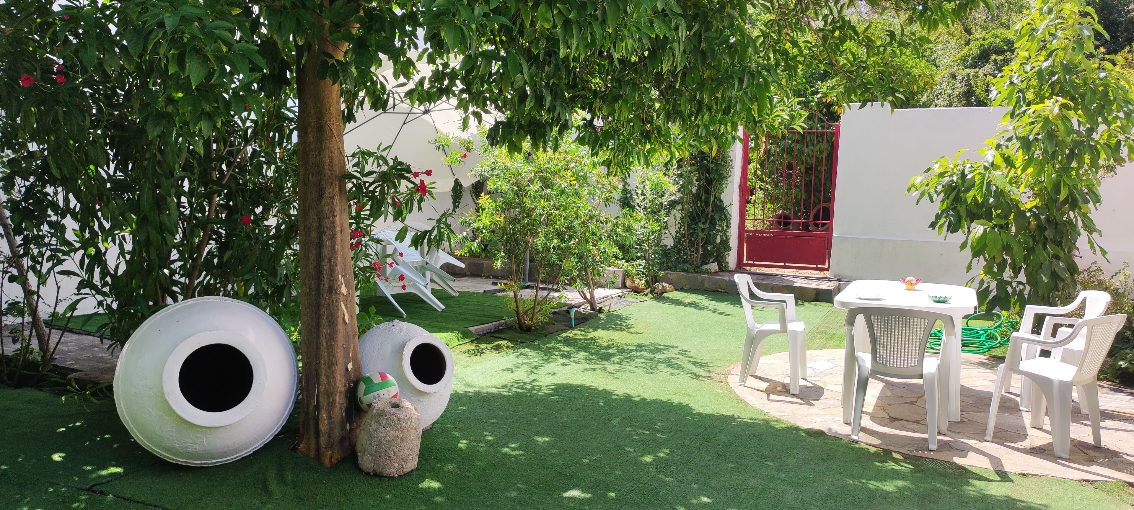 Ein Garten mit Kunstgrasanlage, weißen Plastikstühlen, einem Tisch und einem roten Tor.