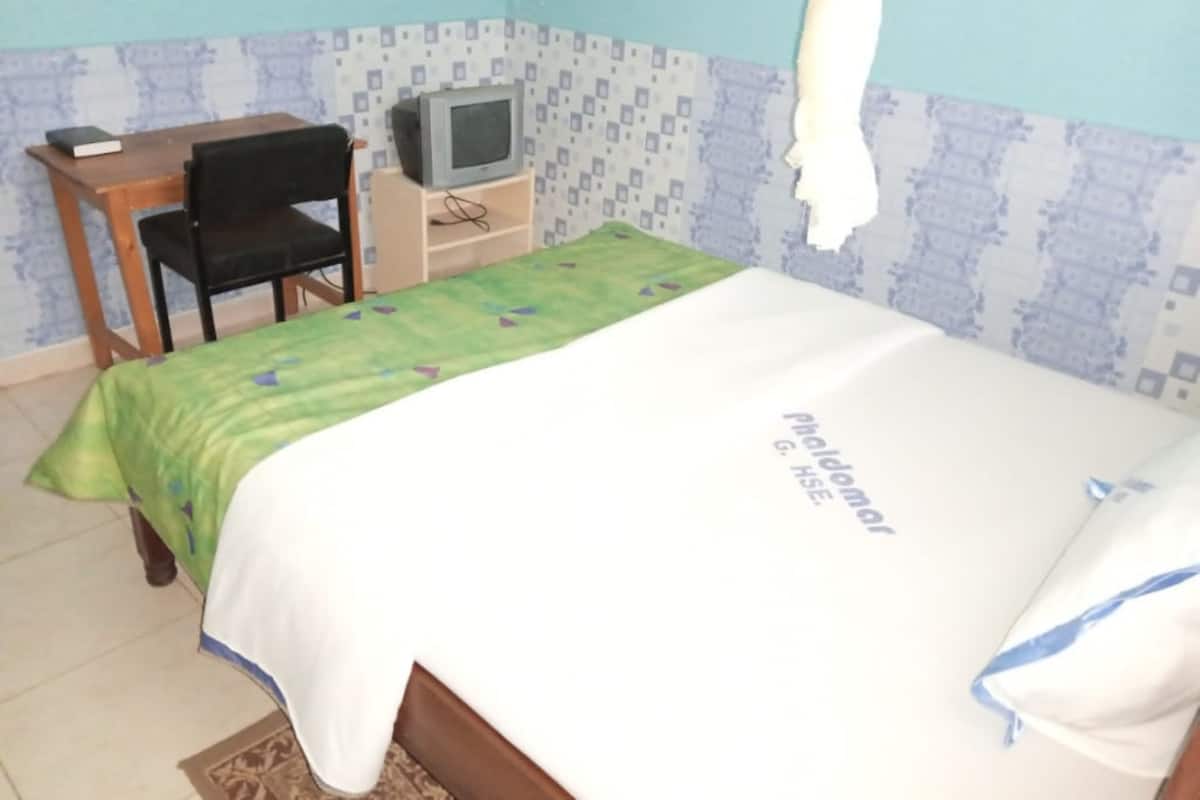 Un dormitorio pequeño con una cama, un escritorio con ordenador, una silla y un televisor.