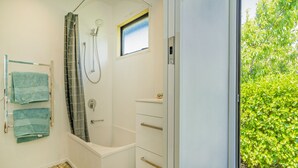A bathroom with a shower, a bathtub, a window, and a towel rack with towels. - Bay Coast Happy Place - Cooks Beach Holiday Home (Cooks Beach)