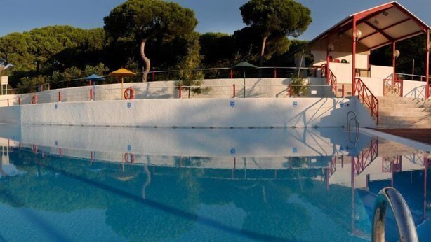 Ein Schwimmbecken mit freiem Blick auf die Umgebung, darunter eine überdachte Sitzgelegenheit und Treppen zu einem Gebäude.