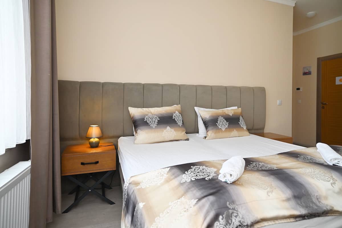 A neatly made bed with a patterned bedspread, two decorative pillows, a bedside lamp, and a wooden nightstand.