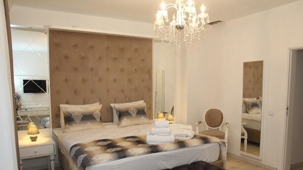 A modern bedroom with a large bed, a bedside table, a chair, a mirror, and a chandelier.