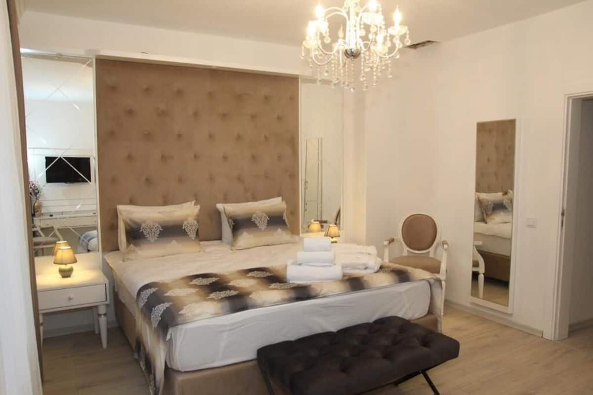 A bedroom with a large bed, a chandelier, a mirror, and a bedside table with a lamp.