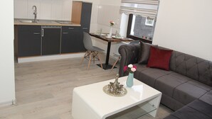 A modern kitchen with dark cabinets, a dining area with a table and chairs, and a living room with a sofa and a coffee table.