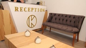 A reception area with a reception desk labeled "RECEPTION," a brown tufted sofa, and a wooden table with decorative glass objects.