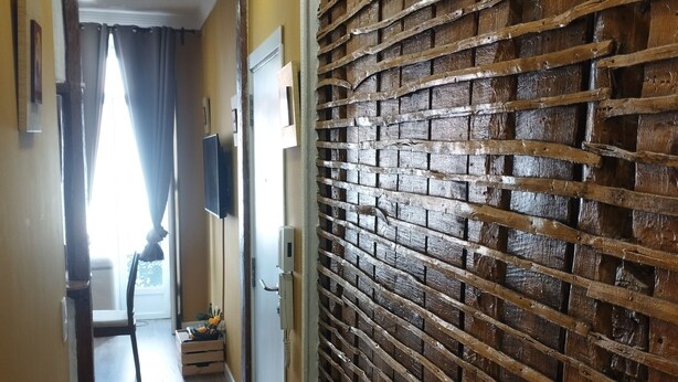 Un pasillo con persianas de madera, un televisor montado en la pared y una puerta que da a una habitación.