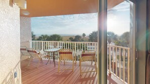 Ein Balkon mit Tisch und Stühlen, Blick auf den Strand und einen klaren Himmel.